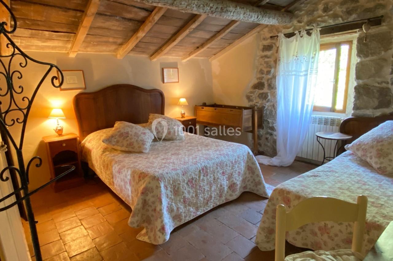 Chambre rustique avec lit double, lit simple, murs en pierre, plafond en bois et lumière naturelle provenant d'une fenêtre.