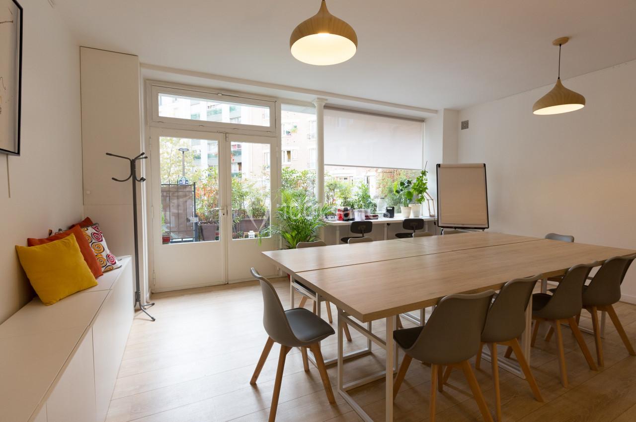 Salle de réunion lumineuse avec grande table en bois, chaises grises, tableau blanc et vue sur une terrasse végétalisée.