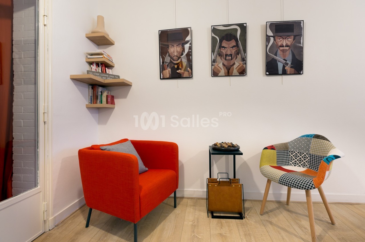 Deux fauteuils colorés, une table avec un sac et des décorations, trois affiches au mur dans un salon moderne.
