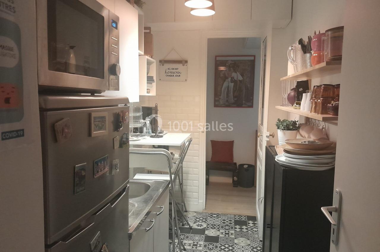 Cuisine étroite avec électroménagers, étagères murales, carrelage au sol et éclairage suspendu.