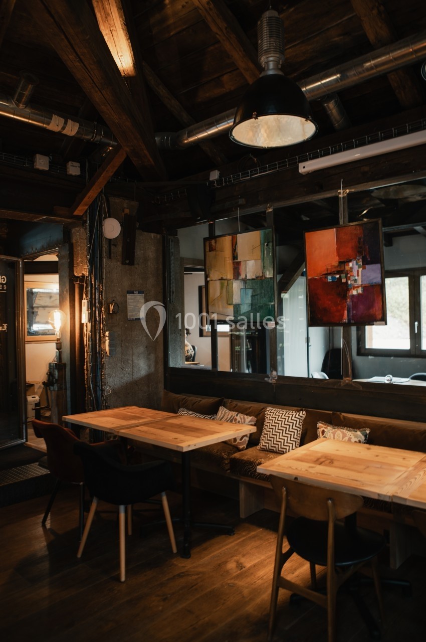 Intérieur d'un café chaleureux avec tables en bois, chaises noires et décorations artistiques suspendues.