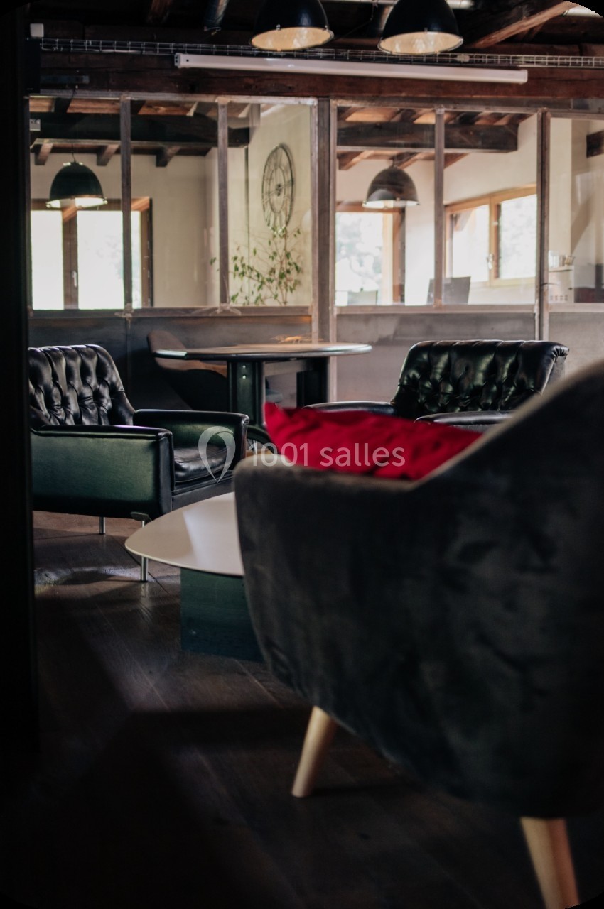 Espace intérieur avec fauteuils en cuir, table basse et grandes fenêtres laissant entrer la lumière naturelle.