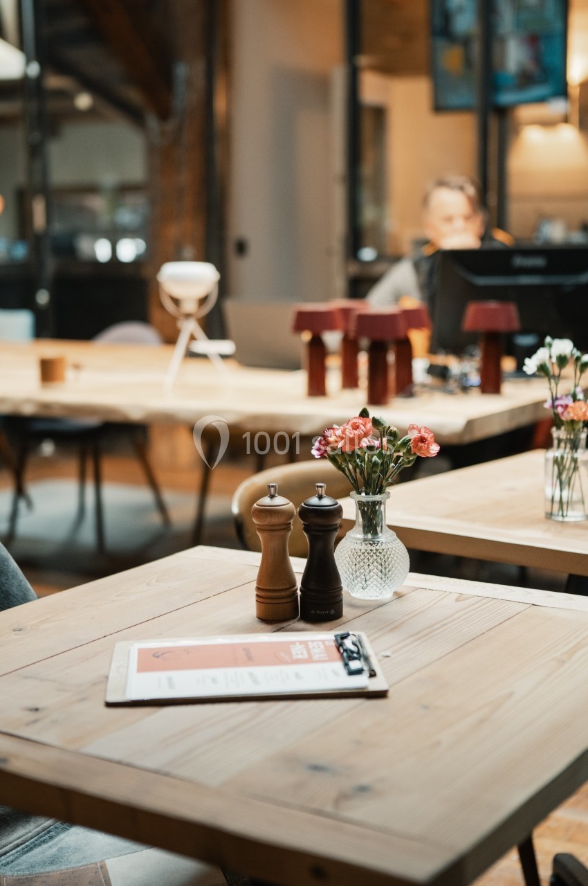 Salle de restaurant avec tables en bois, vase de fleurs, moulins à épices et menu posé au premier plan.