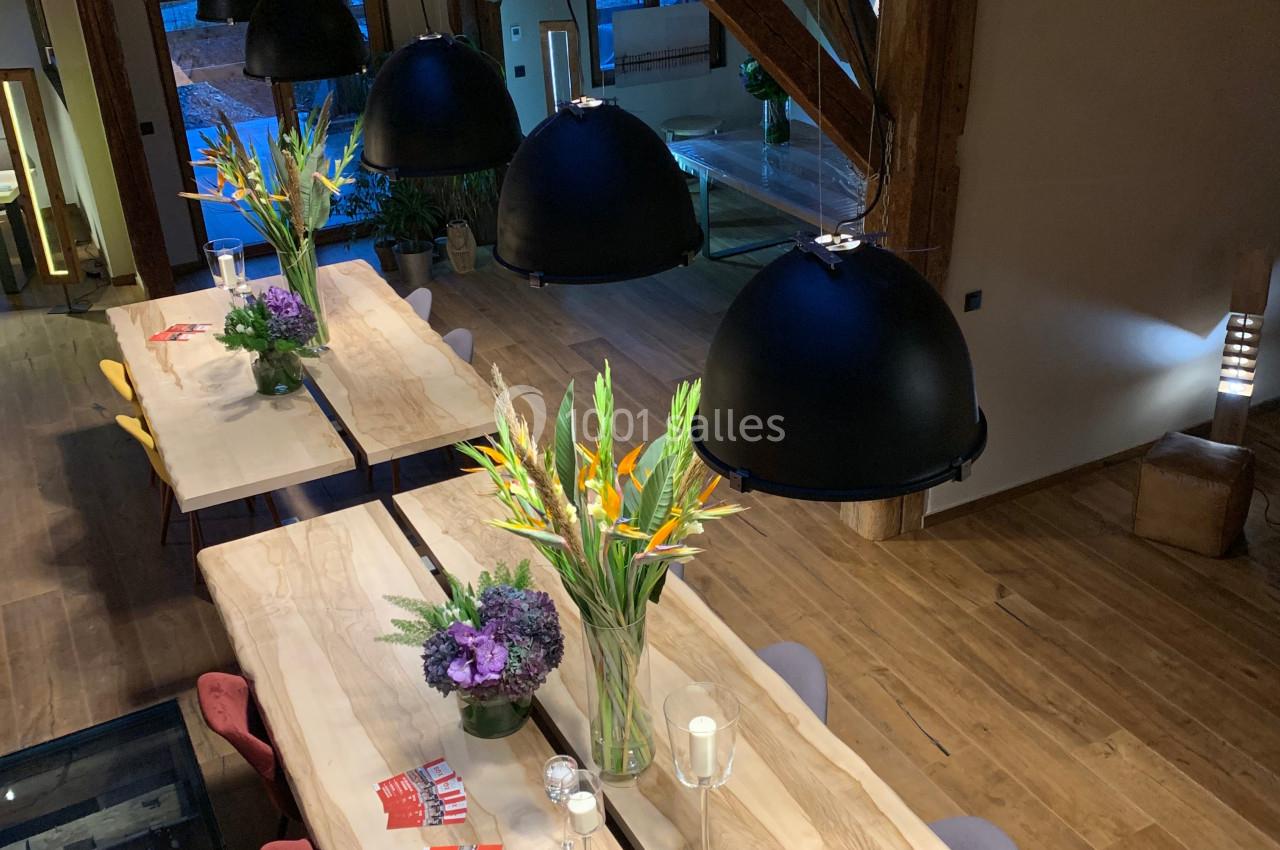 Salle à manger avec de longues tables en bois, décorées de bouquets de fleurs et éclairées par des suspensions noires.