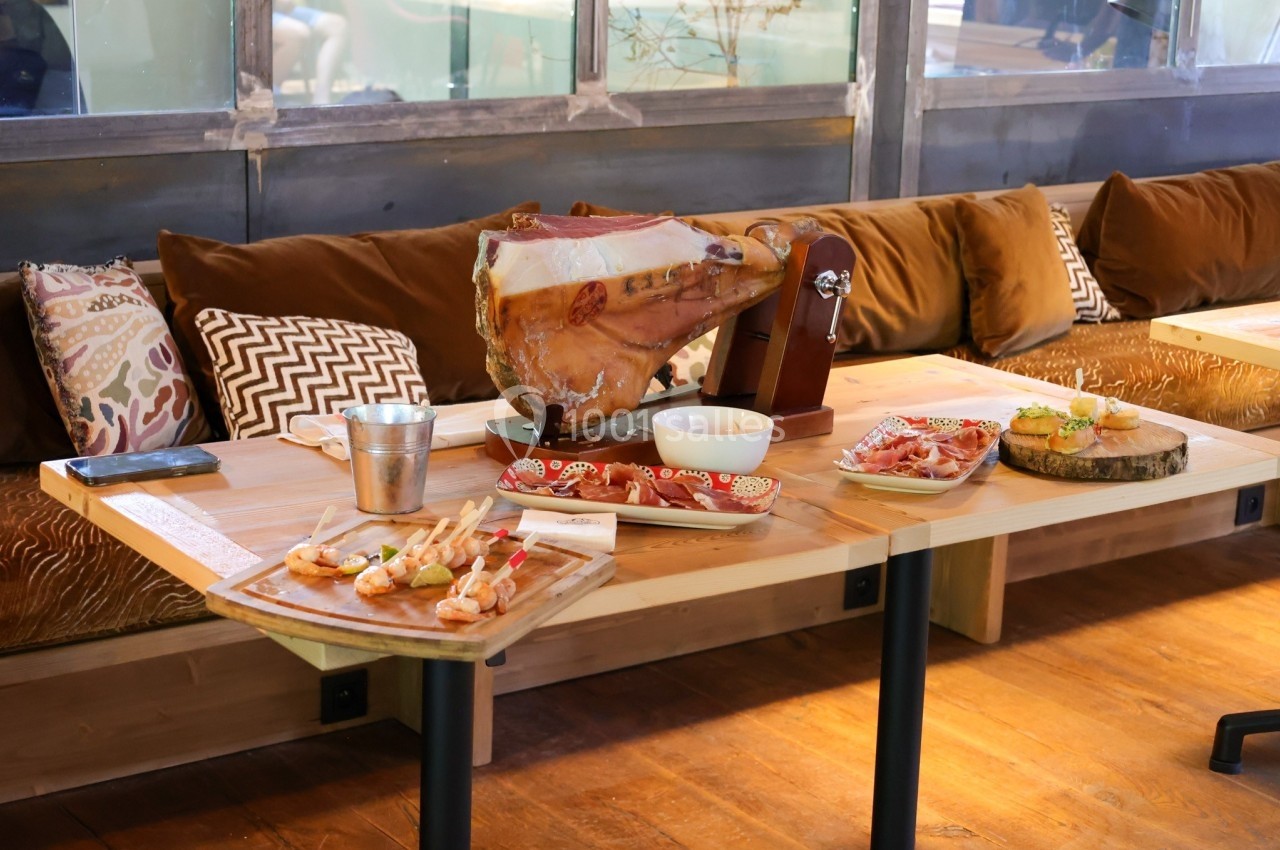 Plateau de charcuterie avec un jambon entier sur support, tapas et accompagnements disposés sur une table en bois.