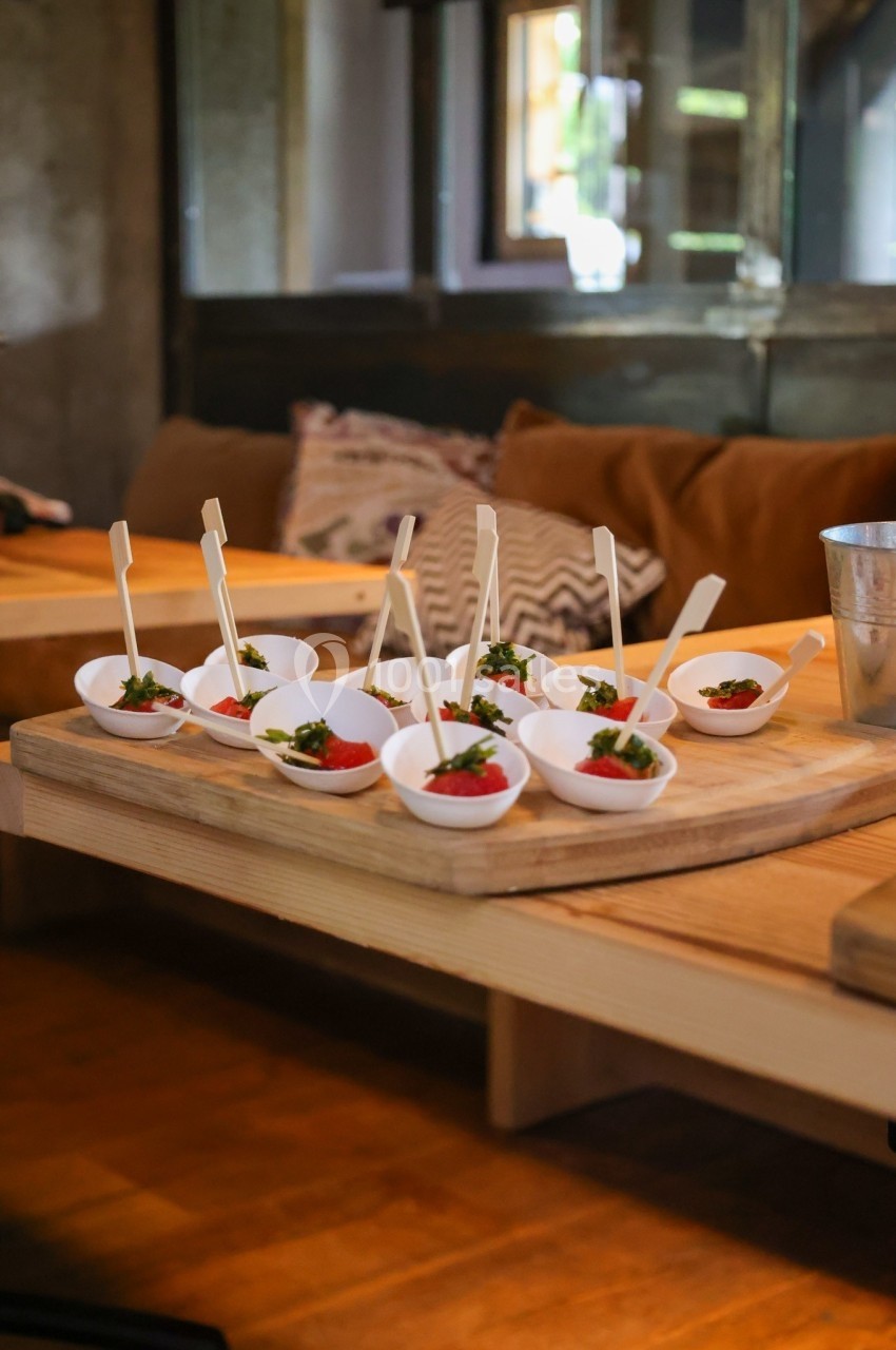 Petites portions de nourriture servies dans des coupelles blanches avec des piques, disposées sur une planche en bois.