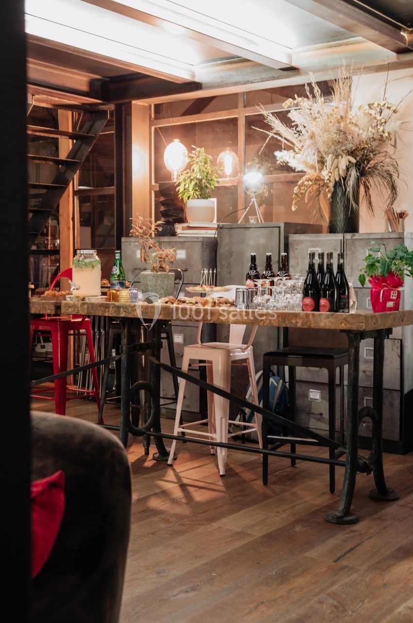 Table en bois avec boissons, plantes et décorations dans un intérieur chaleureux avec éclairage tamisé.