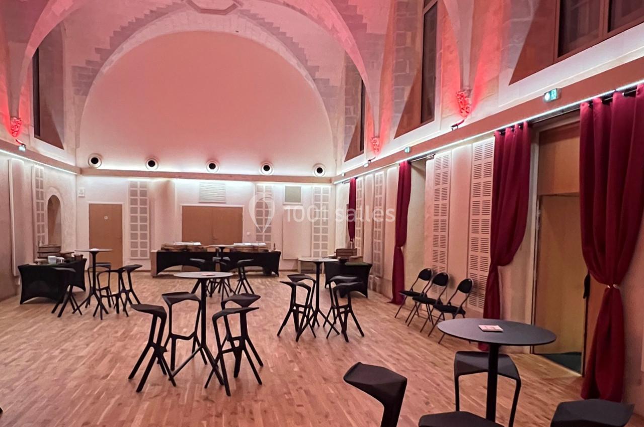 Salle spacieuse avec parquet, tables hautes noires, chaises modernes et éclairage tamisé aux tons rouges.