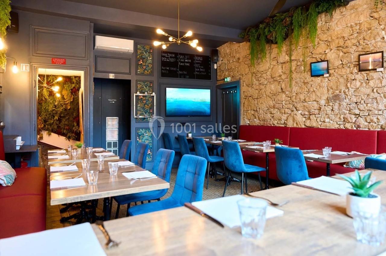 Salle de restaurant lumineuse avec murs en pierre, tables dressées, chaises colorées et décoration végétale.
