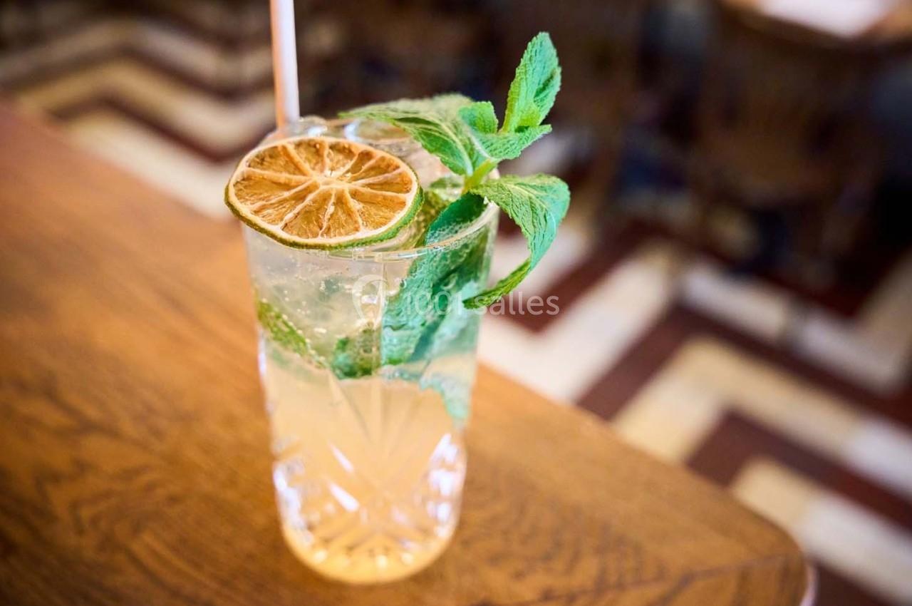 Verre de cocktail garni de menthe fraîche et d'une tranche de citron séché, posé sur une table en bois.