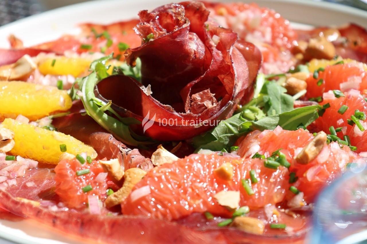 Assiette de carpaccio de viande séchée garnie de roquette, agrumes, ciboulette et éclats de noix.