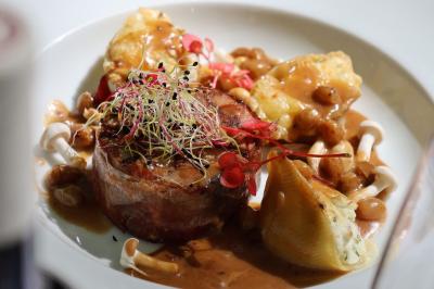 Plat gastronomique composé de viande enroulée, légumes, champignons, sauce brune et garniture de pousses.
