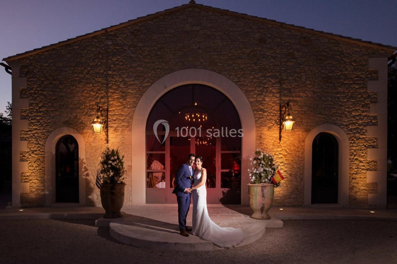 Un couple en tenue de mariage pose devant un bâtiment en pierre éclairé à la tombée de la nuit.