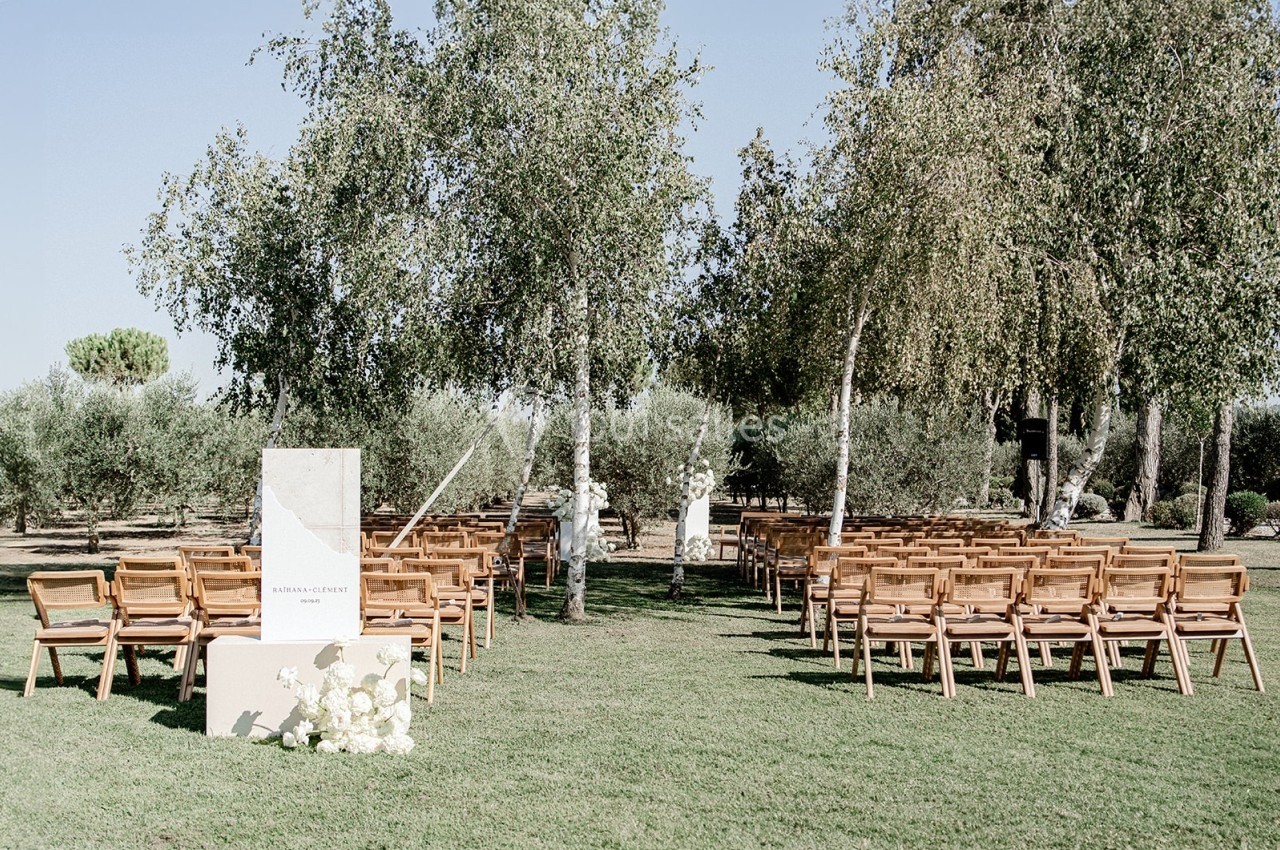 Chaises en bois disposées en rangées sur une pelouse entourée d'arbres, préparées pour une cérémonie en plein air.