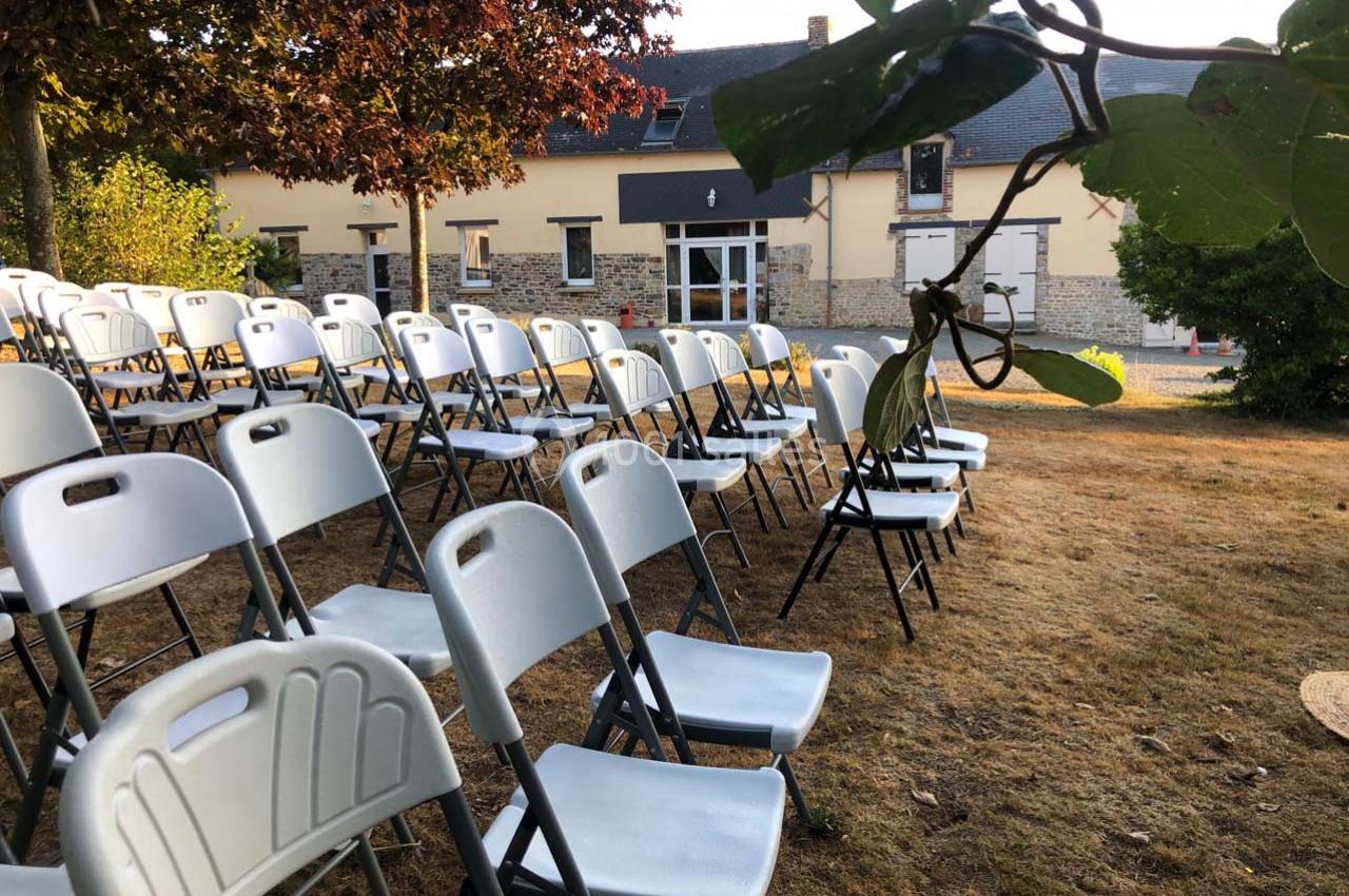 Chaises blanches pliantes disposées en rangées sur une pelouse devant un bâtiment en pierre.