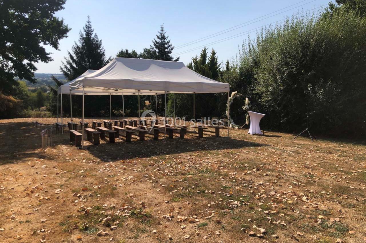 Tente blanche montée dans un espace extérieur avec des bancs en bois disposés pour un événement.