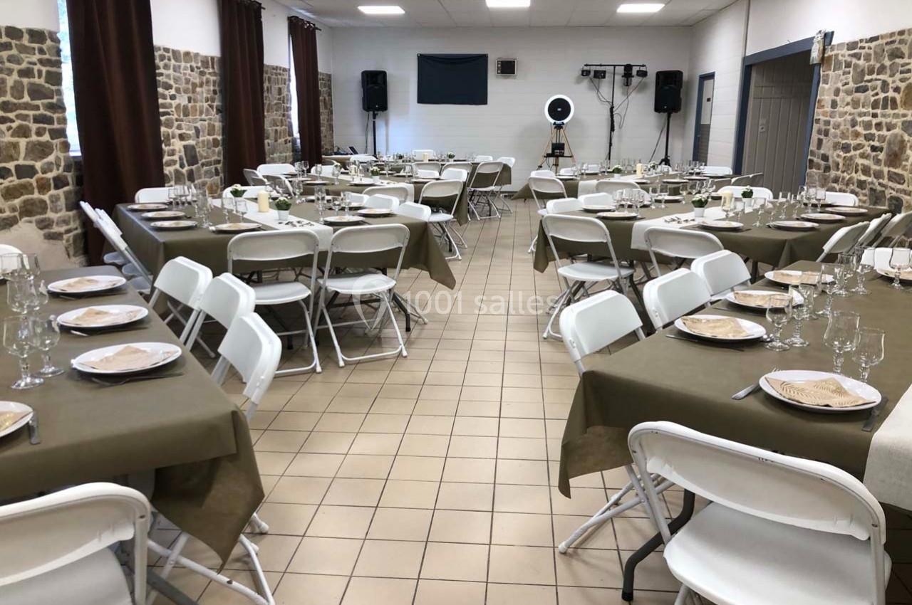 Salle de réception aménagée avec des tables rectangulaires dressées, nappes vertes et chaises blanches pliantes.