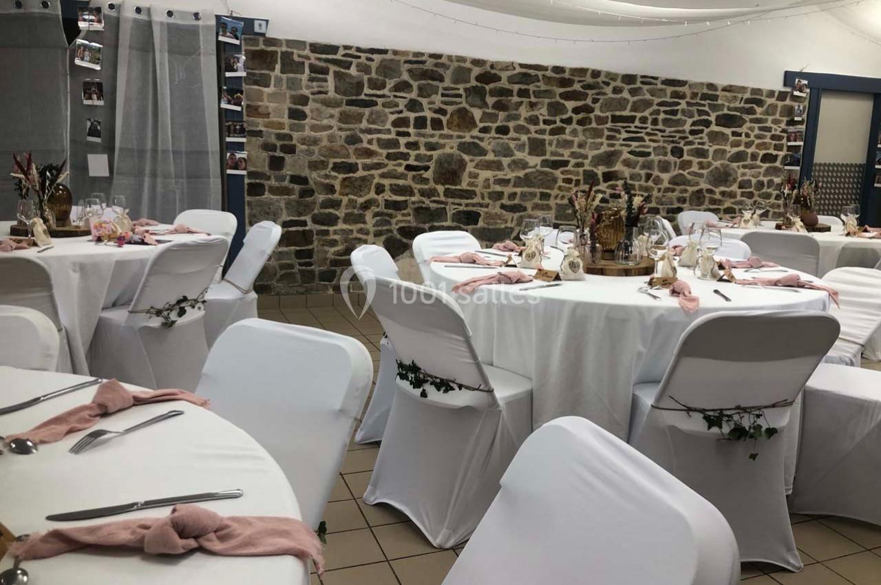 Salle décorée pour un événement, avec des tables rondes couvertes de nappes blanches et des serviettes roses.