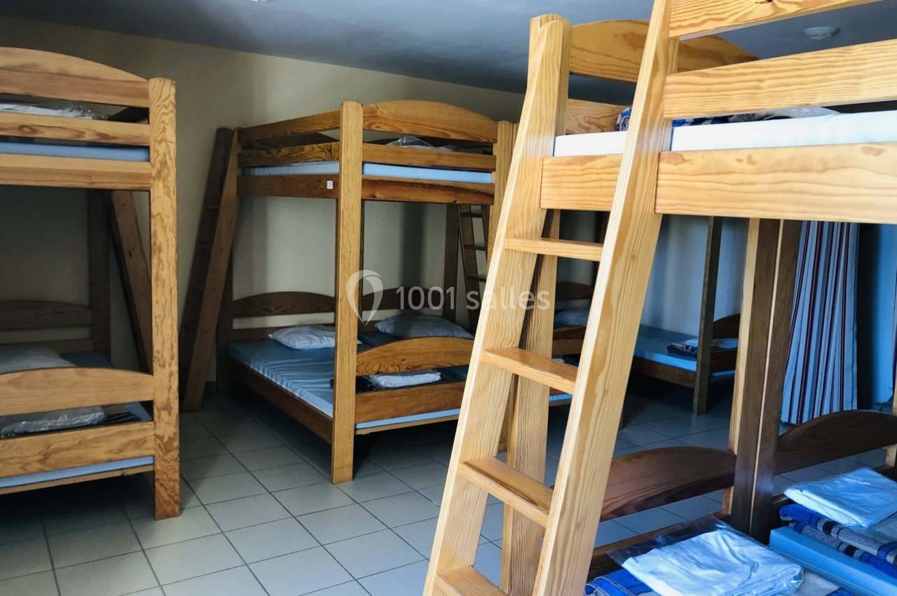 Dortoir avec plusieurs lits superposés en bois, matelas et oreillers, sur un sol carrelé clair.