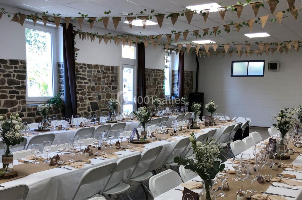 Salle décorée pour un événement avec tables alignées, nappes en toile de jute, vaisselle, fleurs et guirlandes suspendues.