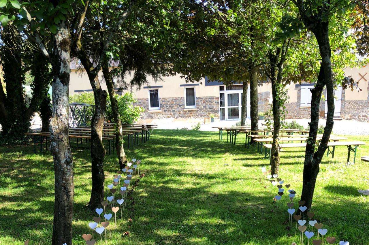 Allée décorée de cœurs en papier menant à des bancs en bois sous des arbres dans un jardin ensoleillé.