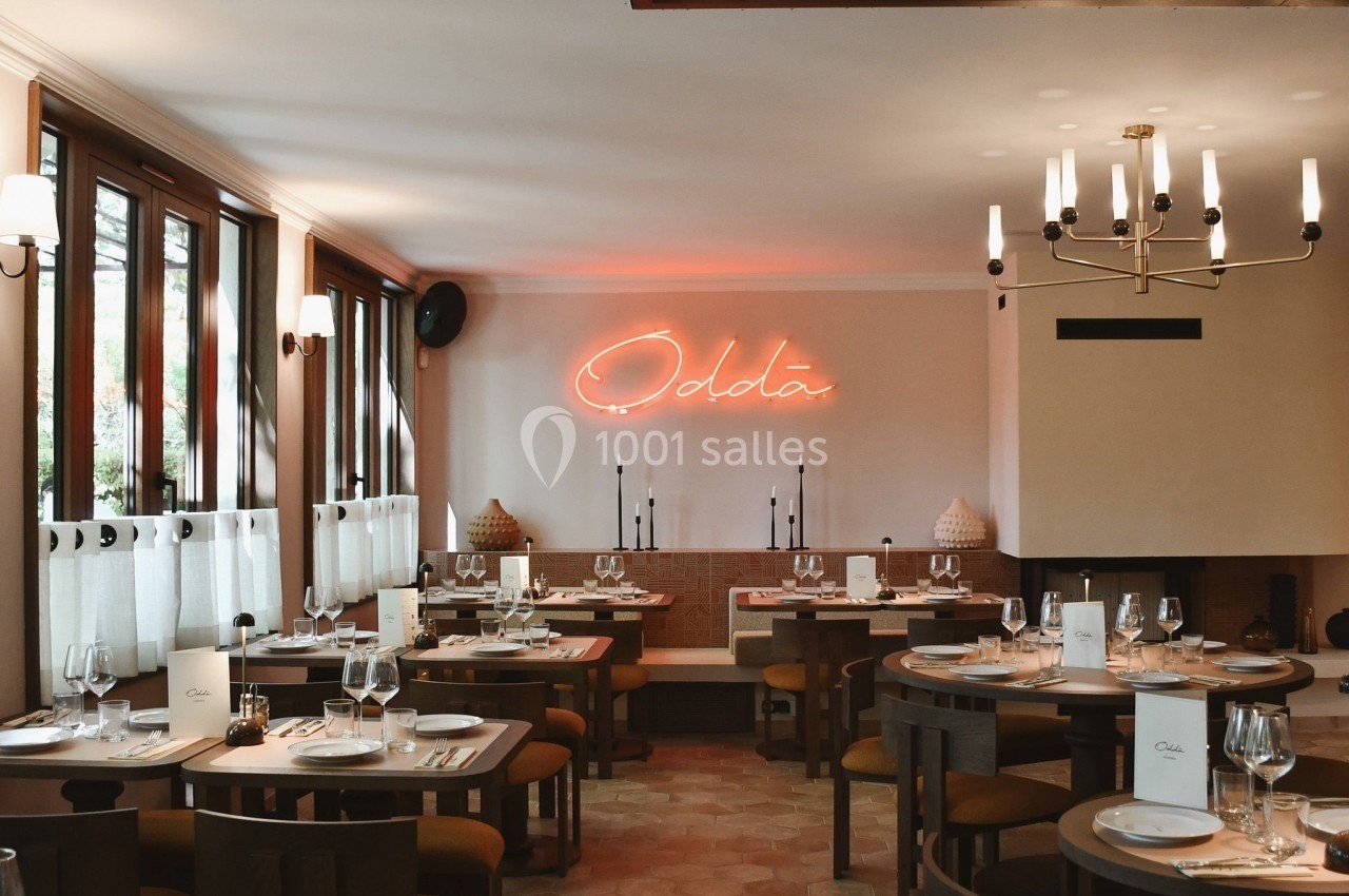 Salle de restaurant élégante avec tables dressées, éclairage chaleureux et enseigne néon au mur.