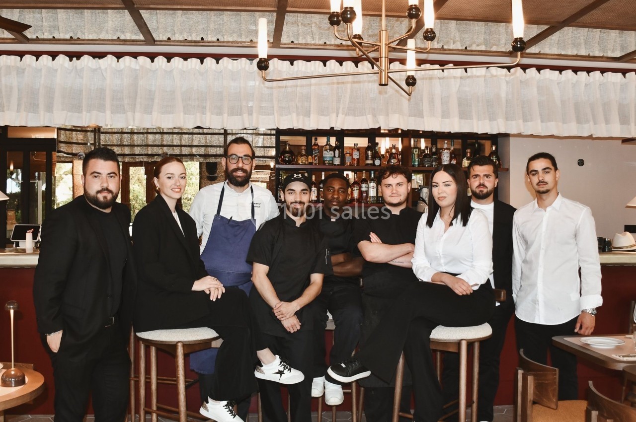 Un groupe de personnes, incluant des serveurs et cuisiniers, posant devant un bar dans un restaurant.