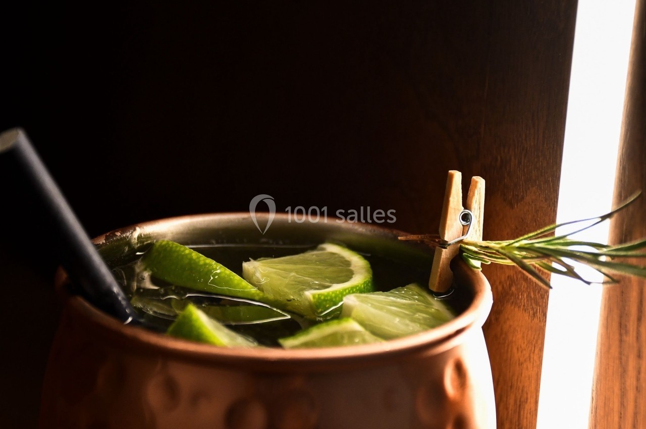 Cocktail servi dans une tasse en cuivre avec des tranches de citron vert, une branche de romarin et une paille noire.