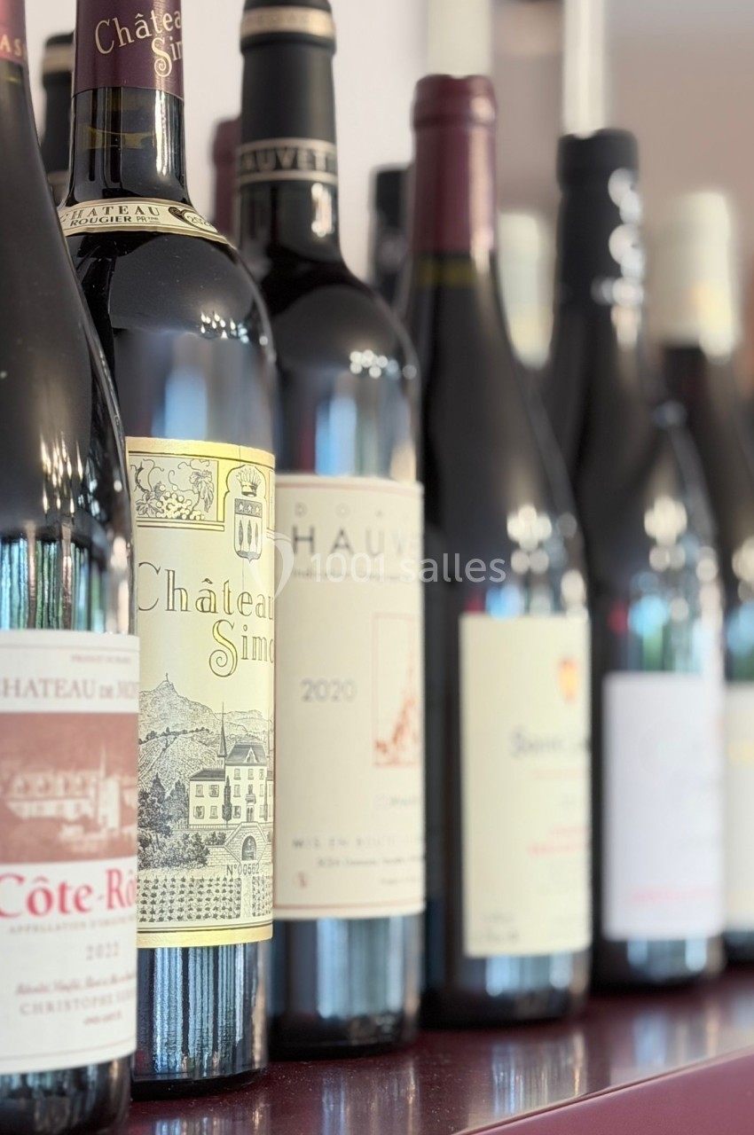Bouteilles de vin rouge et blanc alignées sur une étagère, avec étiquettes visibles.