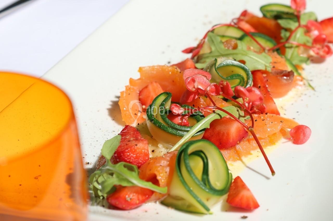 Assiette de saumon fumé garnie de légumes frais, fraises et herbes, présentée sur une table dressée.