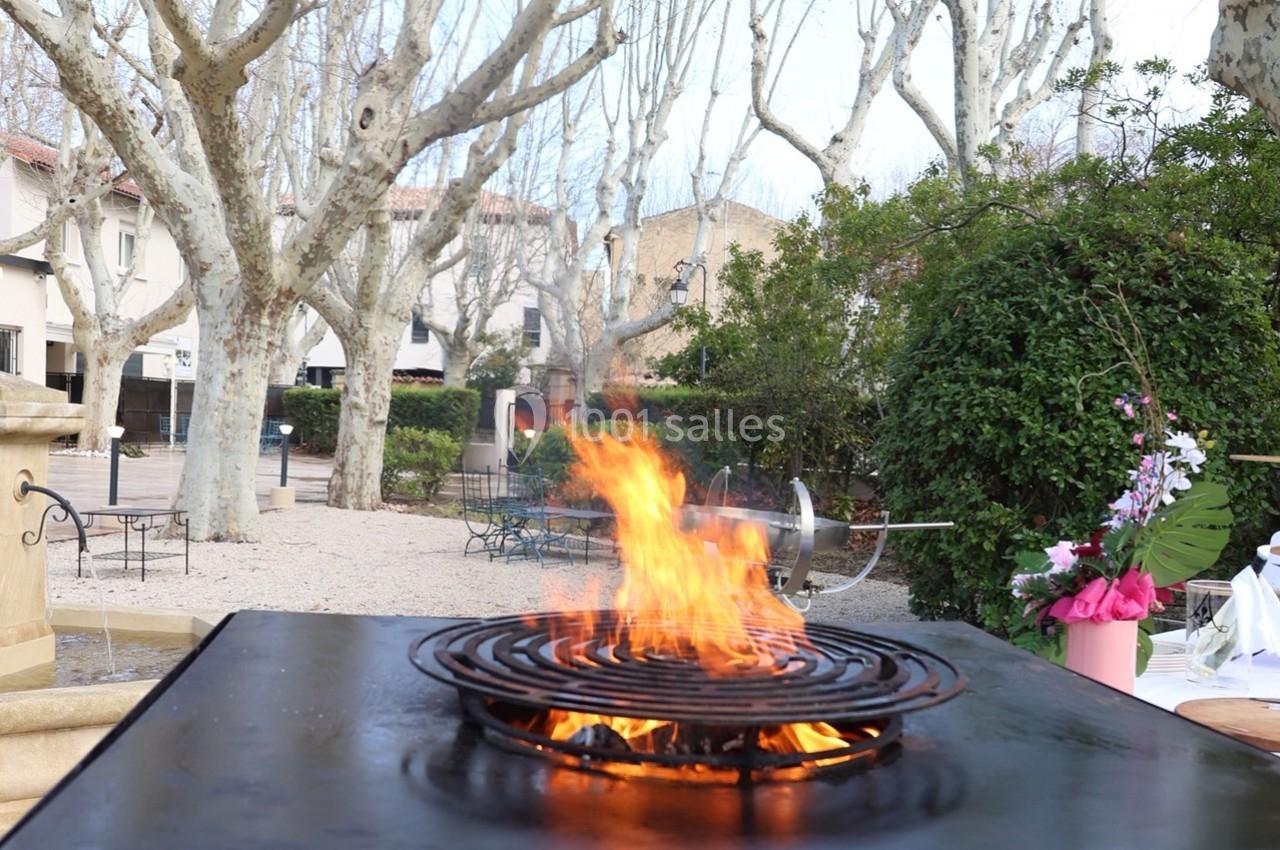 Flammes vives sur un gril en métal dans un espace extérieur entouré d'arbres et de bâtiments.