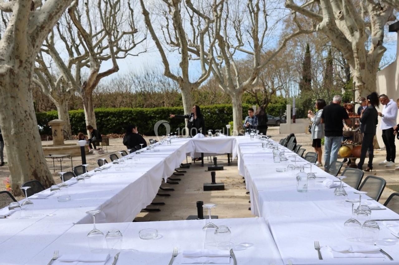 Tables dressées en U avec nappes blanches et couverts, disposées en extérieur sous des arbres sans feuilles.