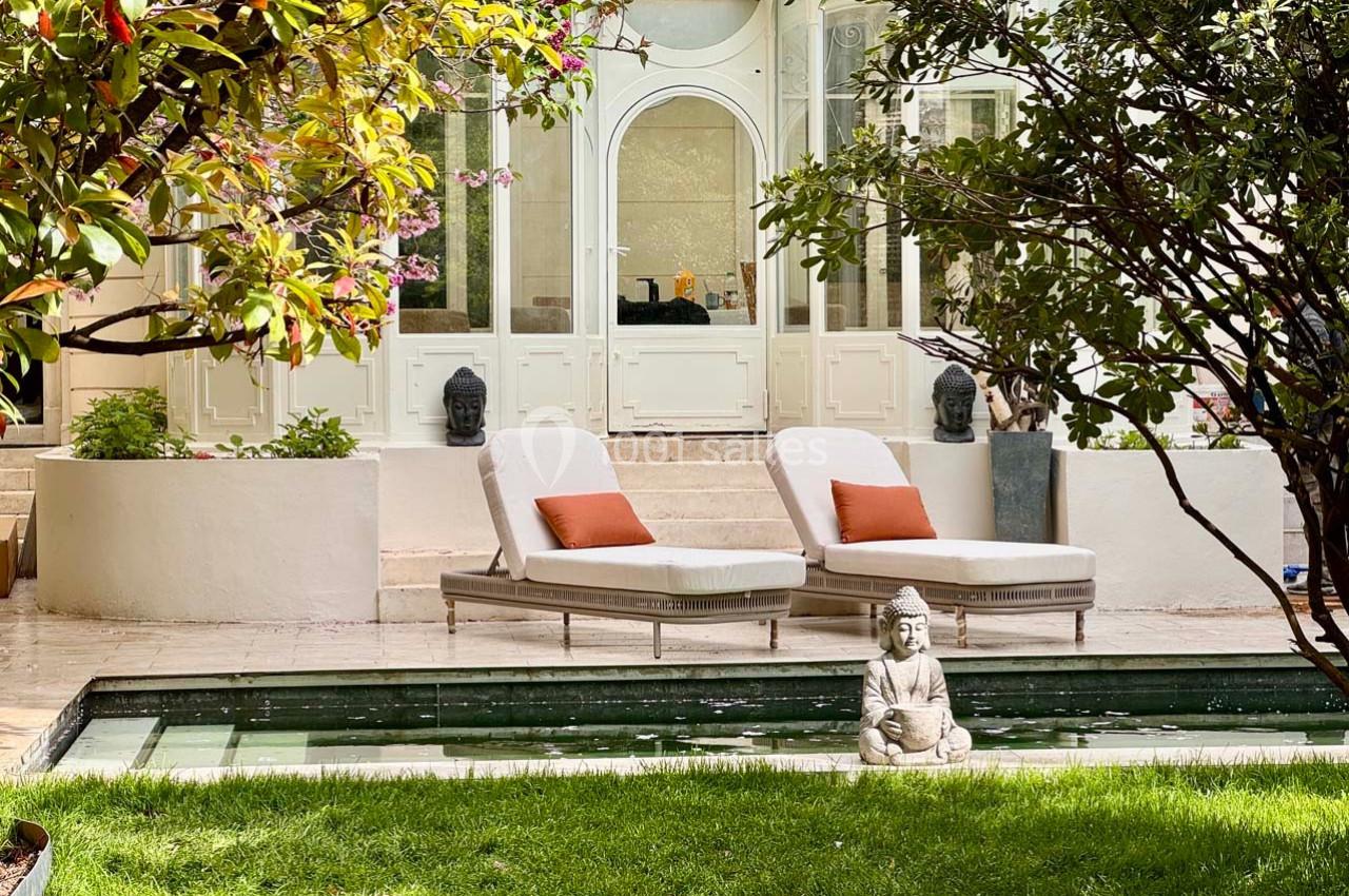 Deux chaises longues avec coussins orange près d'une piscine, entourées de verdure et d'une statue de Bouddha.