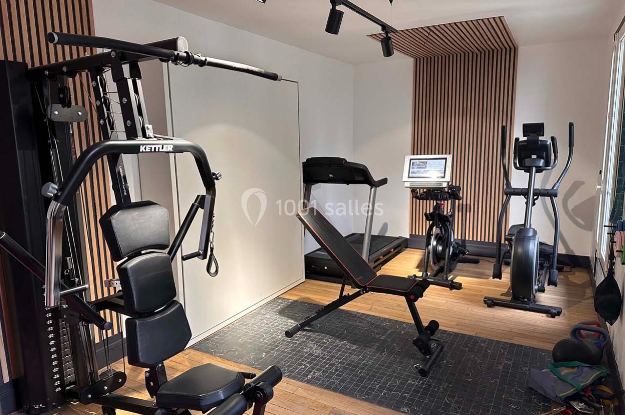 Salle de sport à domicile équipée de machines de musculation, tapis de course, vélo d'appartement et rameur.