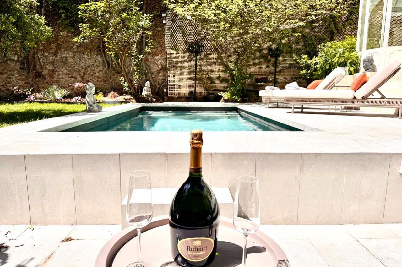 Bouteille de champagne avec deux verres posés sur une table devant une piscine entourée de végétation.