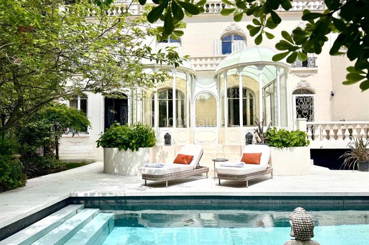 Façade d'une maison élégante avec véranda, transats et piscine entourée de verdure.