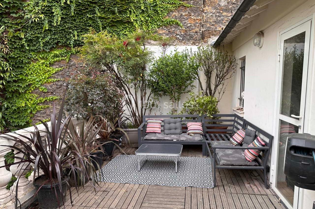 Terrasse avec mobilier de jardin gris, coussins colorés, plantes en pots et mur recouvert de végétation.