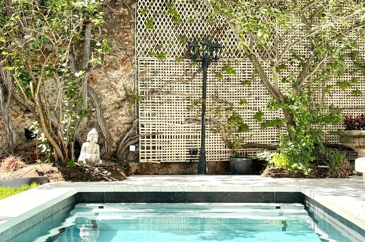 Piscine extérieure entourée de végétation luxuriante, statue décorative et treillis en arrière-plan.