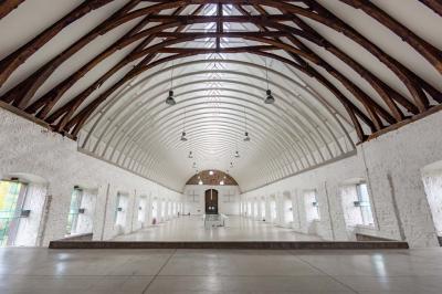 Salle avec des murs en pierre et poutres apparentes, aménagée pour une cérémonie avec des invités assis sur des chaises…