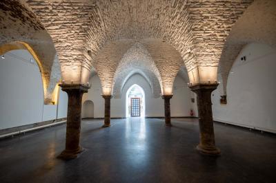 Salle voûtée illuminée par des lumières colorées, remplie de convives assis à des tables lors d'un événement.