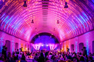 Salle voûtée illuminée par des lumières colorées, remplie de convives assis à des tables lors d'un événement.