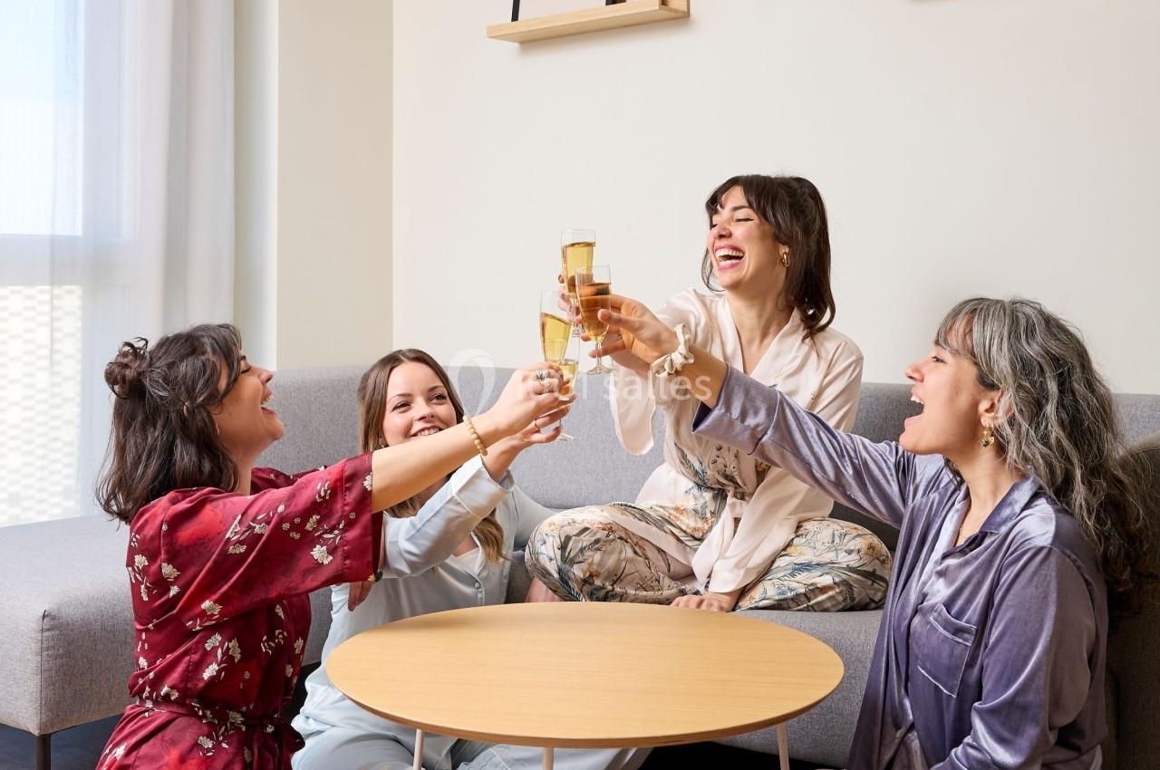 Quatre femmes en pyjama trinquent avec des verres de champagne dans un salon lumineux et convivial.