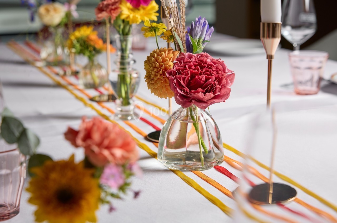 Arrangement de fleurs colorées dans des vases en verre sur une table décorée avec une nappe blanche et un chemin de table…