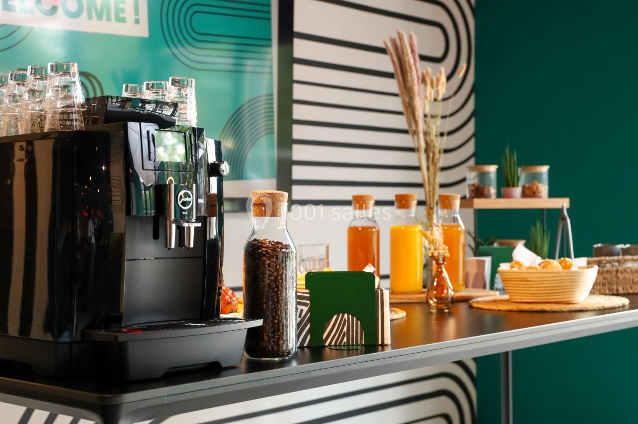 Machine à café automatique sur une table avec des bouteilles de jus, des snacks et une décoration moderne en arrière-plan.