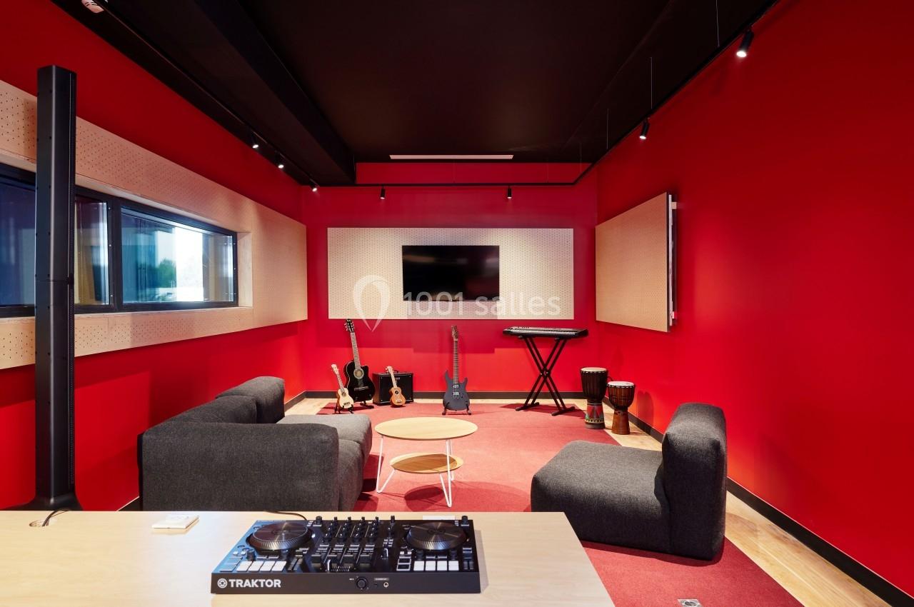 Salle de musique moderne avec murs rouges, instruments variés, fauteuils et table basse sur un tapis rouge.
