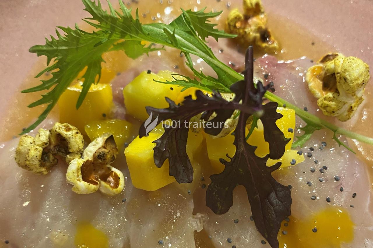 Tranches de poisson cru avec dés de mangue, feuilles de salade, maïs soufflé et graines noires sur une assiette.