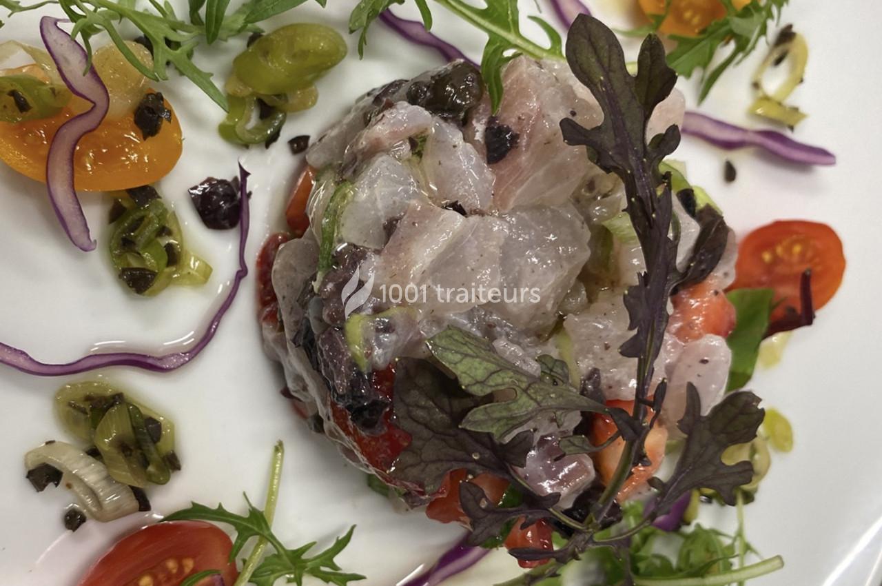 Tartare de poisson cru avec légumes colorés, herbes fraîches et garniture de tomates cerises sur une assiette blanche.