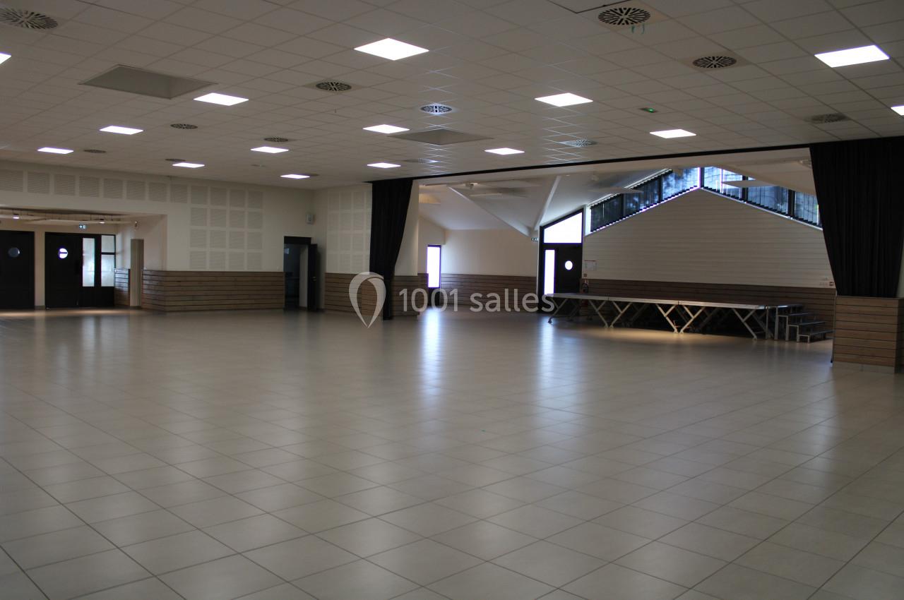 Salle spacieuse avec sol carrelé, murs clairs, plafond à dalles lumineuses et estrade en bois au fond.