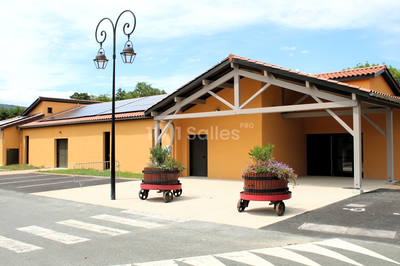 Bâtiment moderne avec façade orange, toit en tuiles, entrée couverte et deux jardinières en tonneaux sur roulettes.