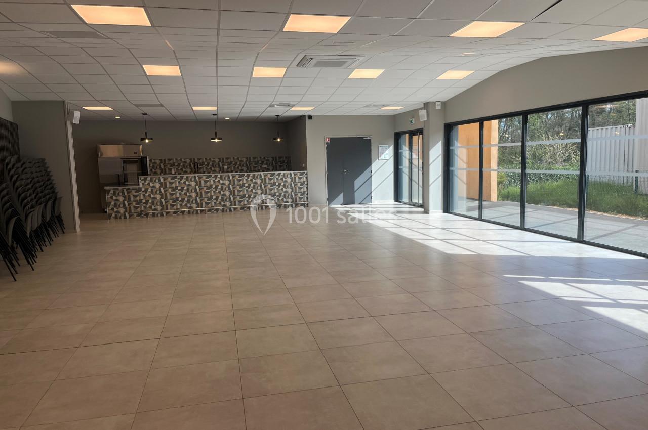 Salle spacieuse avec carrelage clair, baies vitrées, chaises empilées sur le côté et comptoir en fond.